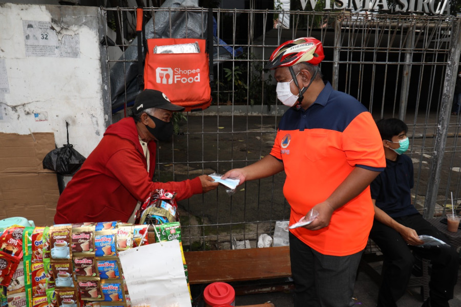 Sekretaris Utama BNPB Lilik Kurniawan (kanan) memberikan masker kepada pedagang kaki lima di Gondangdia, Jakarta, Jumat (11/2).